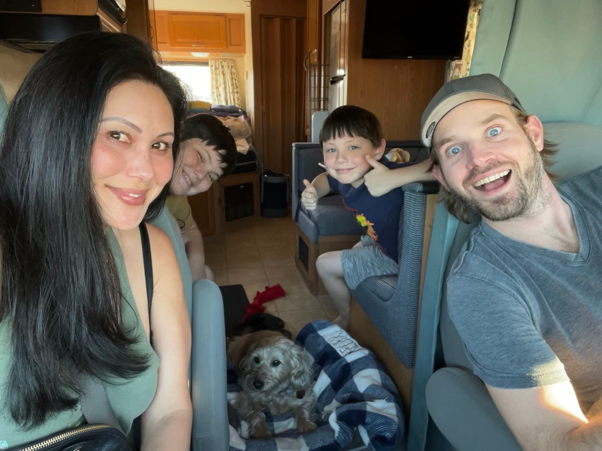 A group of four people and a dog inside a vehicle, smiling and looking at the camera