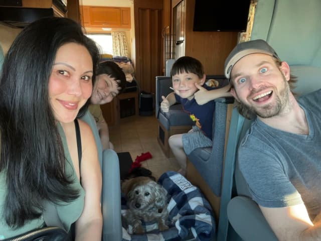 A group of four people and a dog inside a vehicle, smiling and looking at the camera
