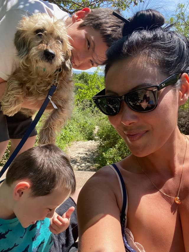 A group selfie featuring a woman wearing sunglasses, two children, and a small dog, all outdoors on a sunny day