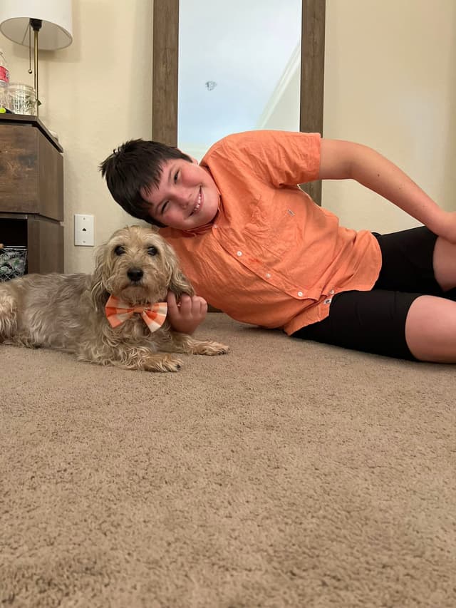A person lying on the floor next to a small dog wearing a bow tie, both in matching orange outfits, in a room with a mirror and a lamp